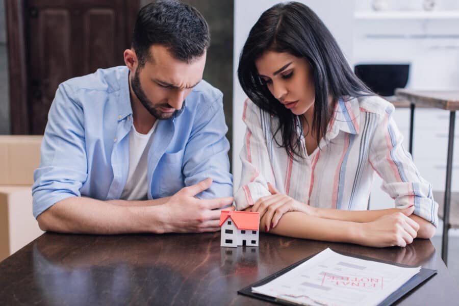 Couple worried about their mortgage with house model and documents.