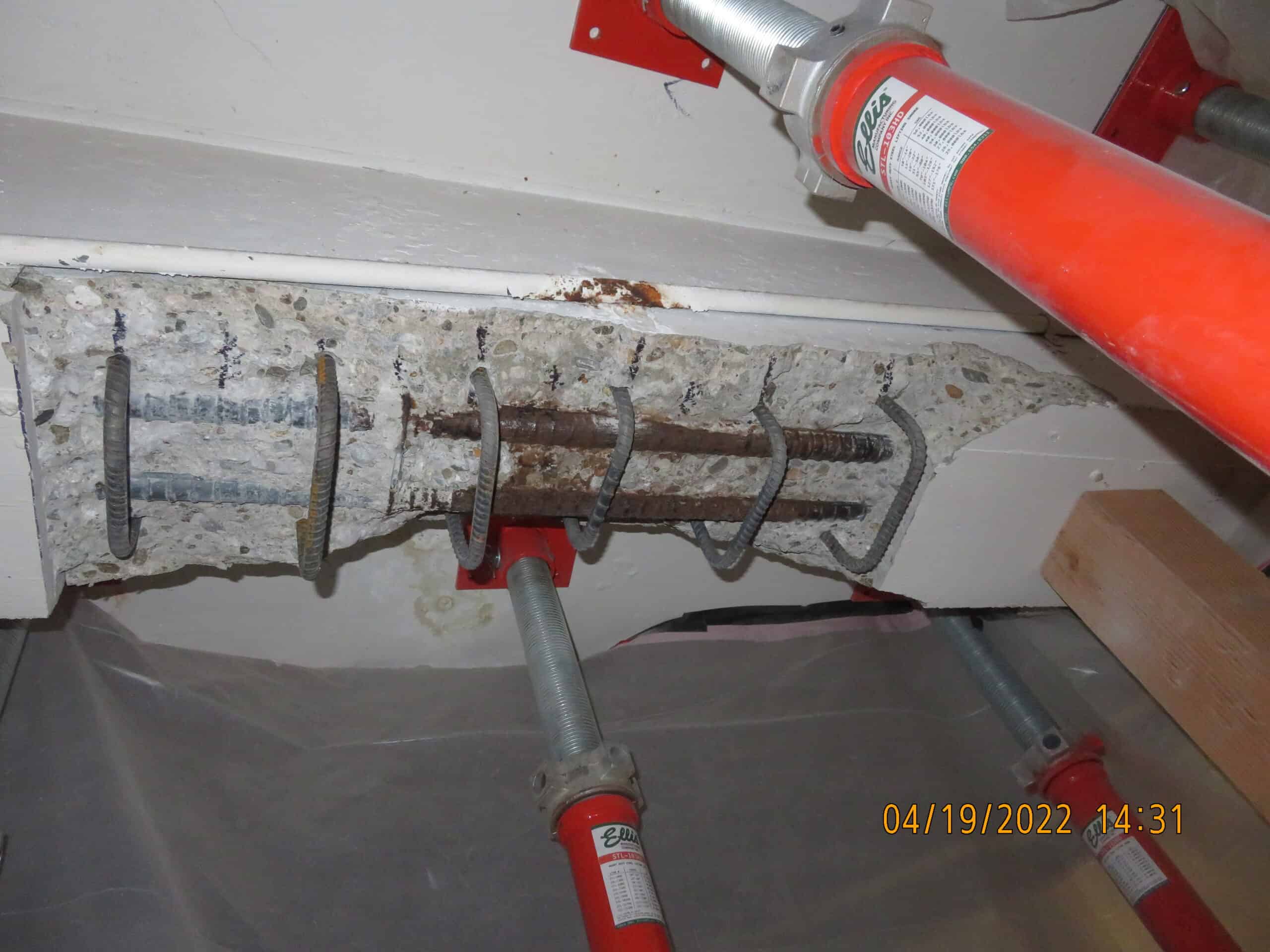 Parking structure beam with concrete chunks falling — Stage 3 spalling caused by rebar corrosion swelling from inside.