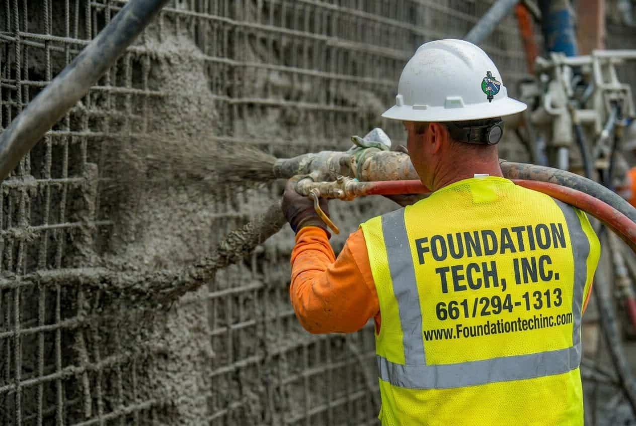 Shotcrete installation on a vertical retaining wall for hillside stabilization.