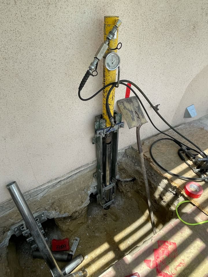 ECP 300 push pier drive stand mounted to residential slab foundation — bracket transfers structural load to pier as it is driven to bedrock